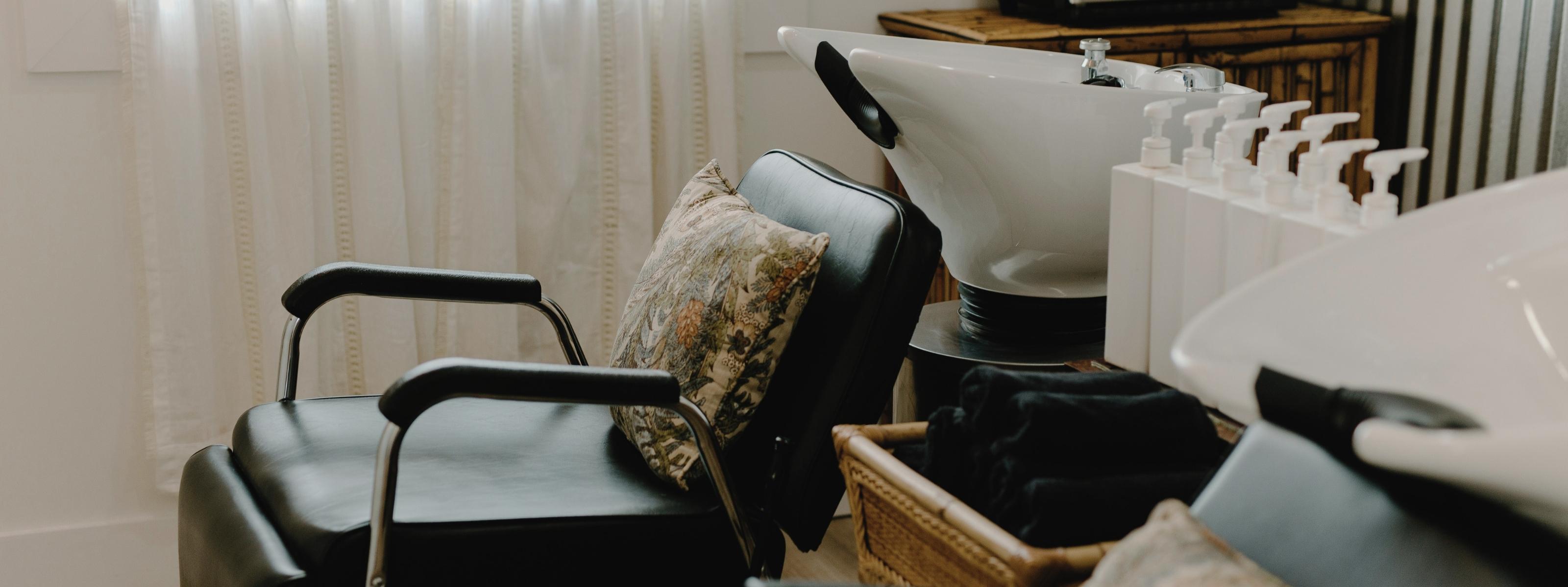 Moderner Friseursalon mit schwarzen Ledersesseln, einem Waschbecken und einem Korb voller schwarzer Handtücher – symbolisiert professionelle Textilien für den Salonbedarf