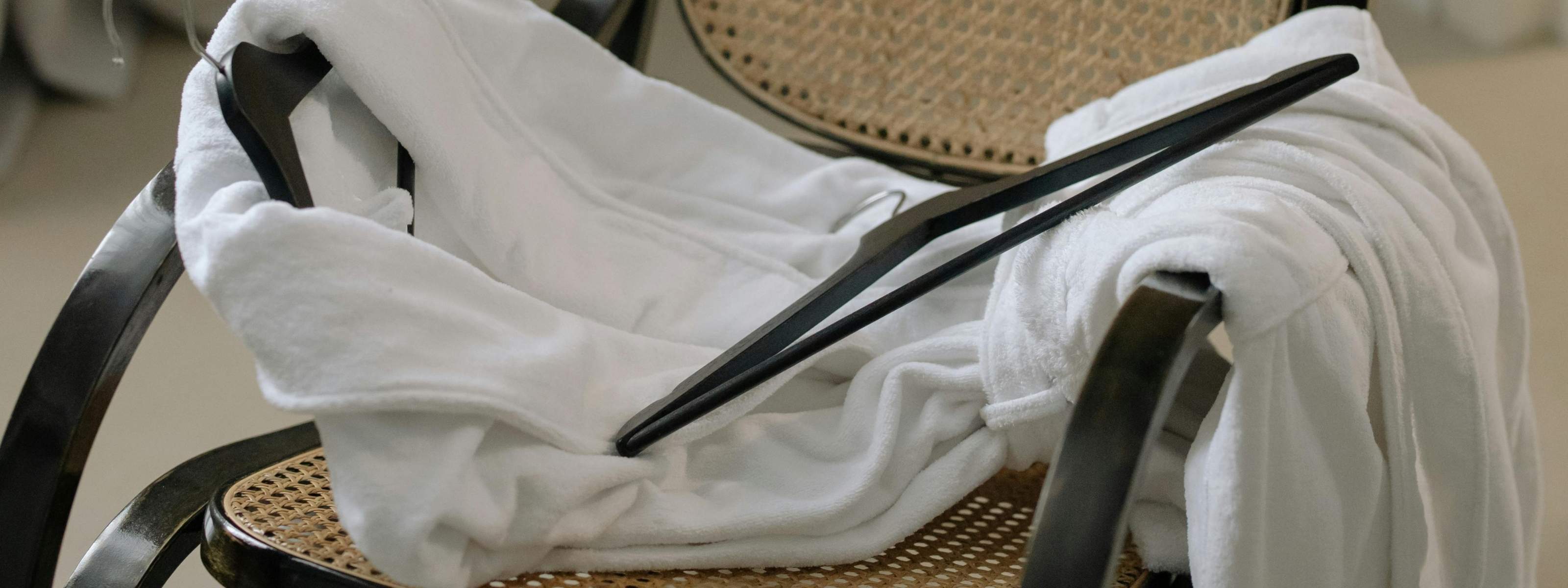 Weißer Bademantel auf einem klassischen Holzstuhl mit Wiener Geflecht, minimalistisch und zeitlos