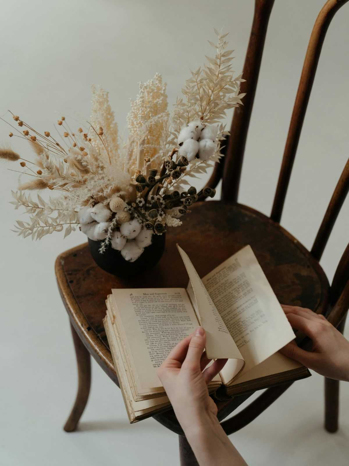 Bouquet aus Trockenblumen, darunter Baumwolle auf einem alten Stuhl, daneben ein altes Buch - Symbol für Tradition