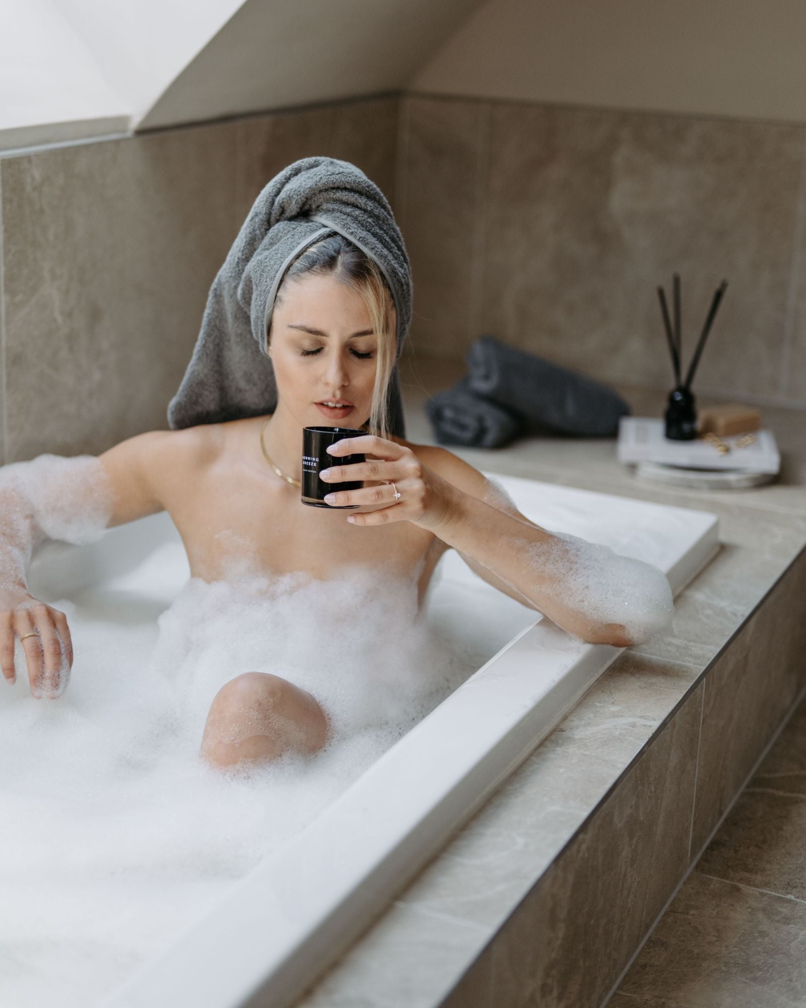 Junge blonde Frau in einer Badewanne mit viel Schaum bedeckt, riechend an einer Duftkerze