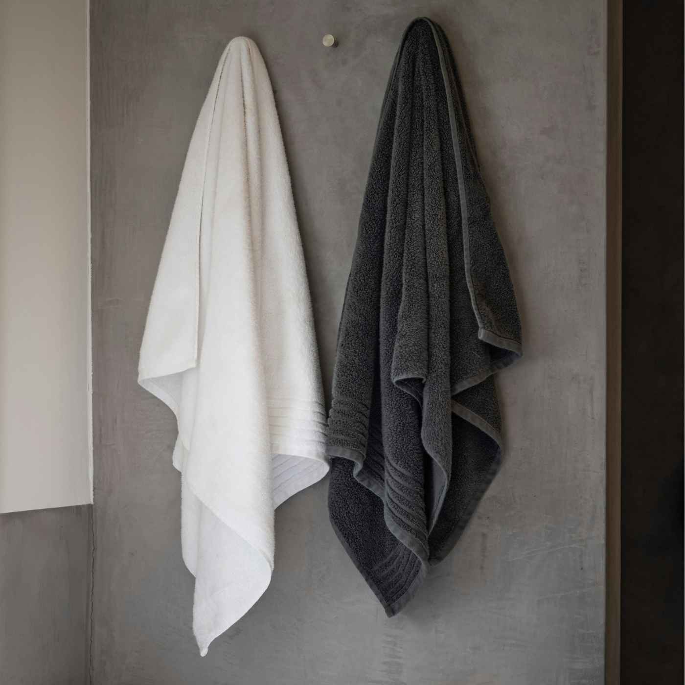 Baumwoll-Frottierhandtücher in weiß und dunkelgrau an Haken hängend in einem Badezimmer