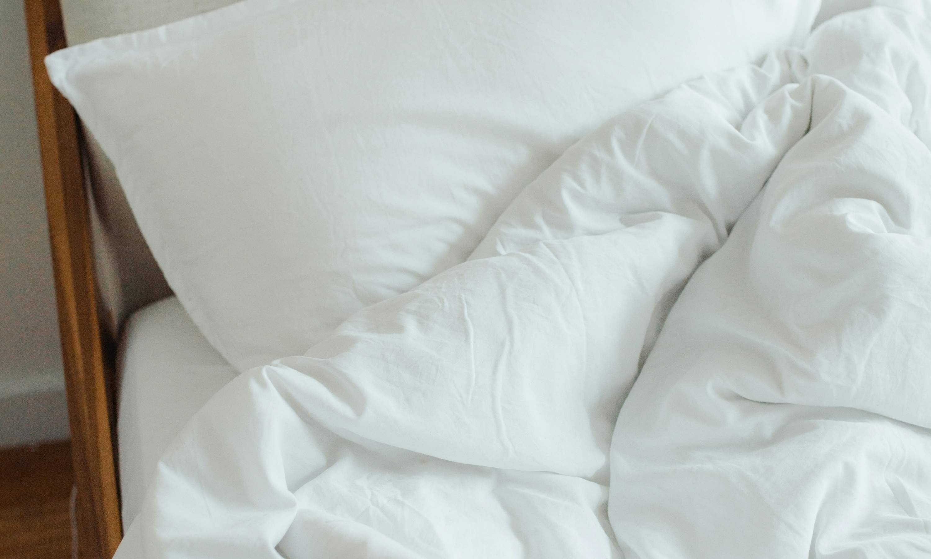 Weiße Bettwäsche aus Baumwolle, locker auf einem Bett arrangiert, mit einem Kissen im Hintergrund