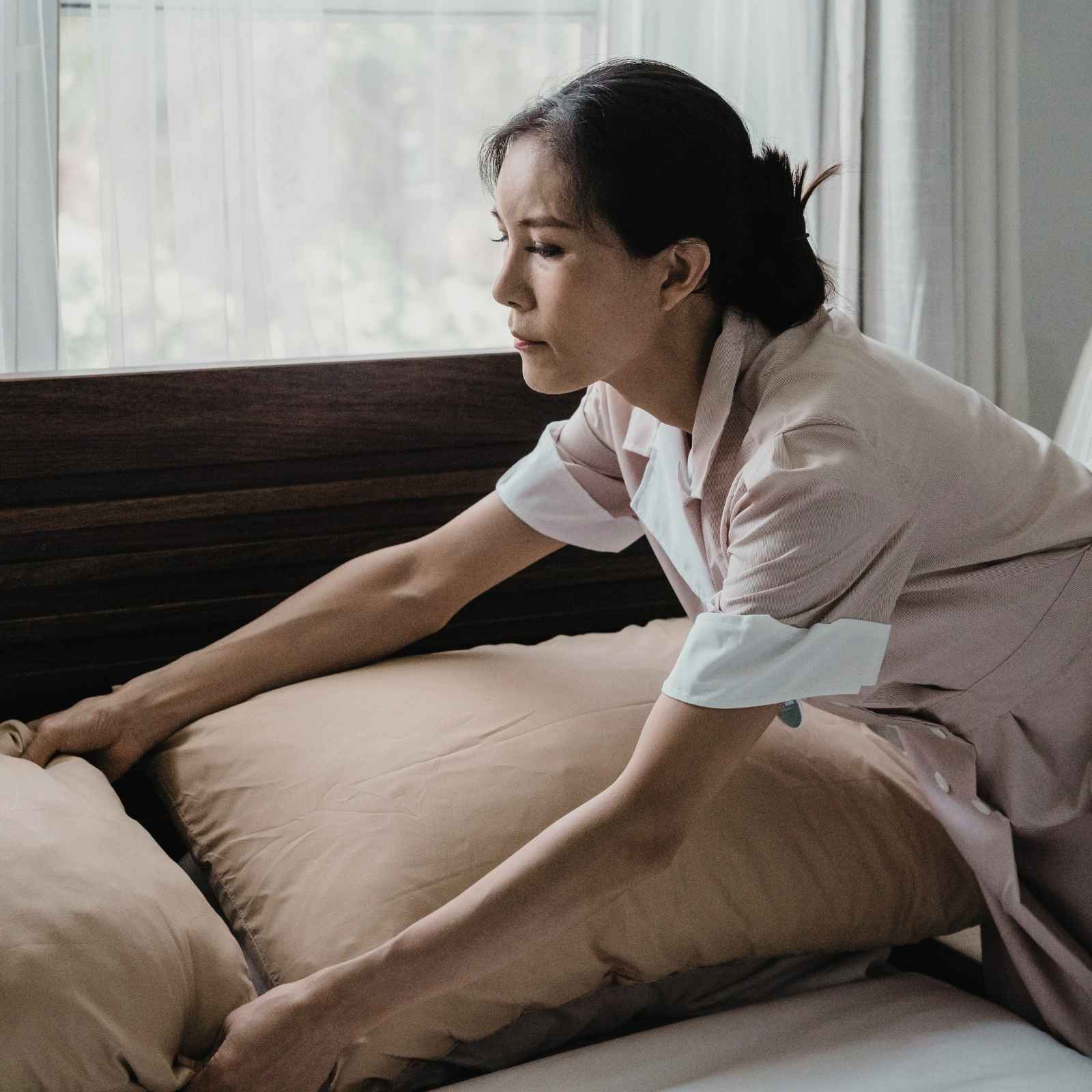 Eine Person legt beigefarbene Bettwäsche auf ein Bett – symbolisiert hochwertige und praktische Heimtextilien für Hotels und Gästehäuser