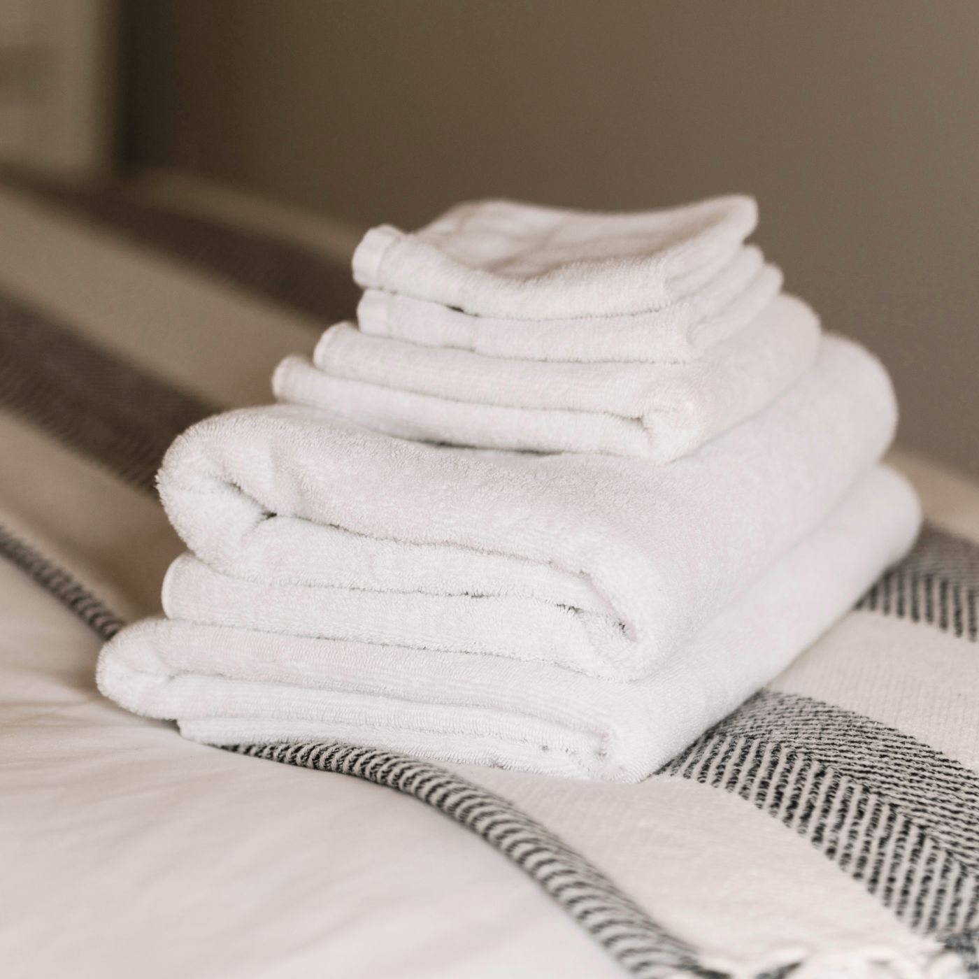 Ein Stapel hochwertiger weißer Handtücher auf einem Bett – repräsentiert die Vielseitigkeit und Anpassungsfähigkeit der Produkte für verschiedene Branchen