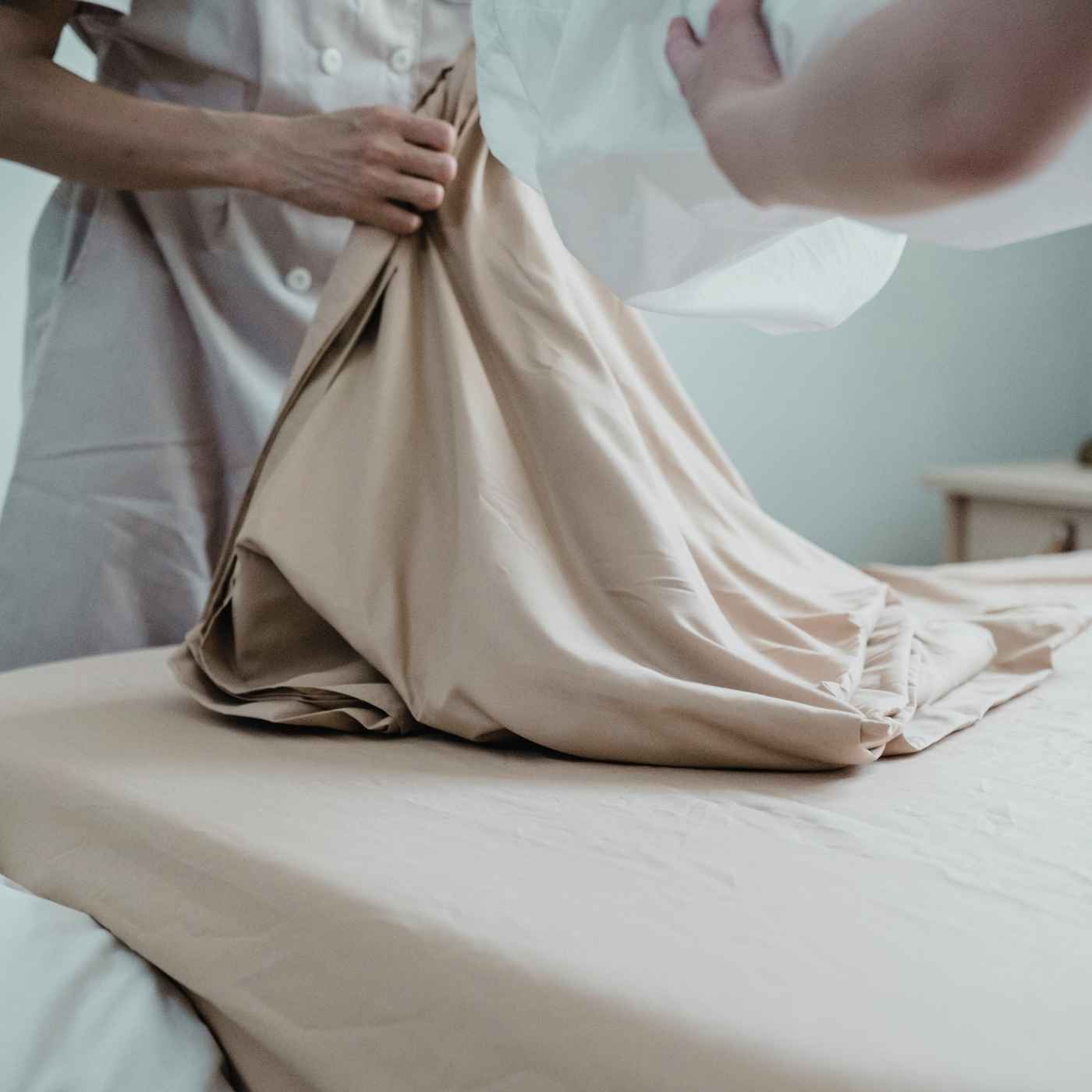  Eine Person legt beigefarbene Bettwäsche auf ein Bett – symbolisiert langlebige Produkte für den professionellen Einsatz